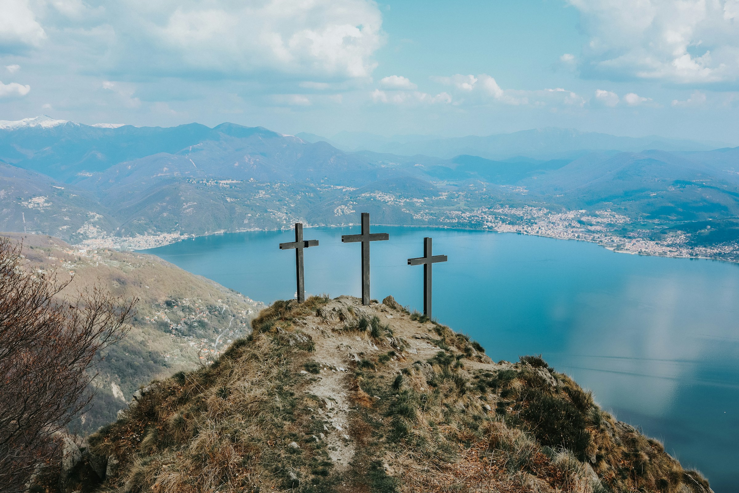 Drei Holzkreuze stehen auf einem Berg über einer Meeresbucht. Im Hintergrund sind Hügel, Dörfer und Berge sichtbar.