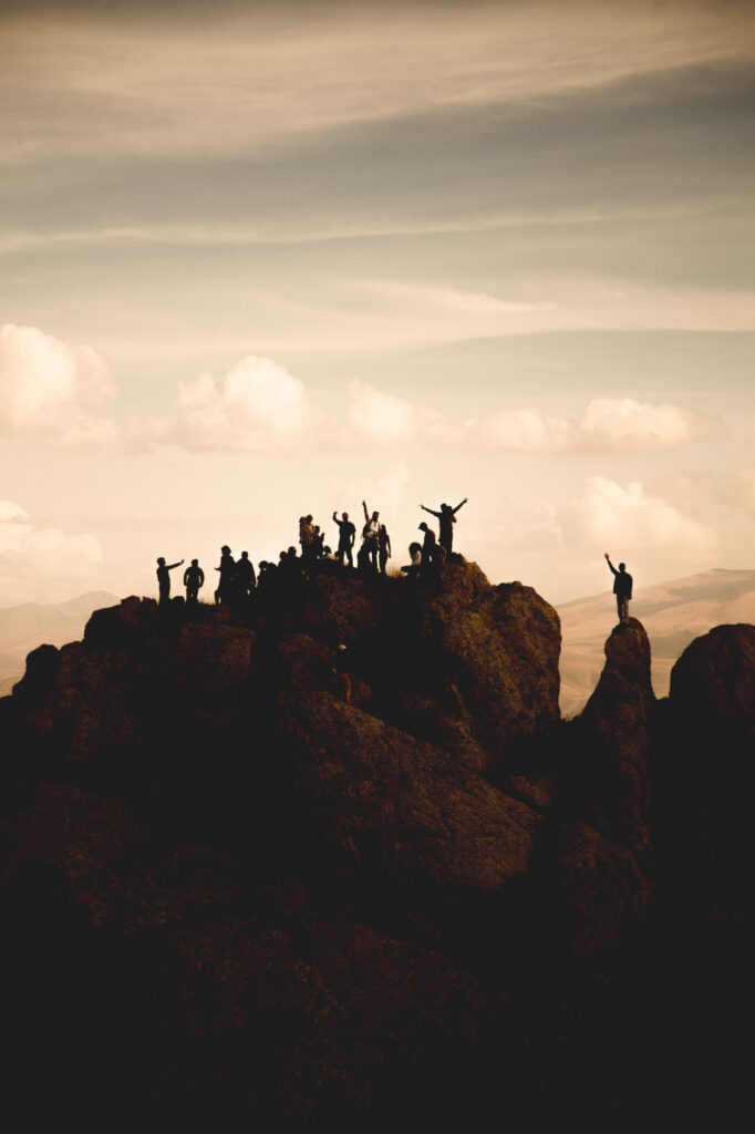Gruppe von Menschen steht als Silhouetten auf einem Berggrat. Einige Personen heben die Arme.