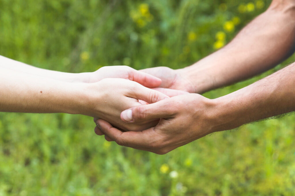 Bild von freepik Zwei Personen halten sich mit beiden Händen an den Händen, Hintergrund mit grüner Wiese und unscharfer Vegetation.