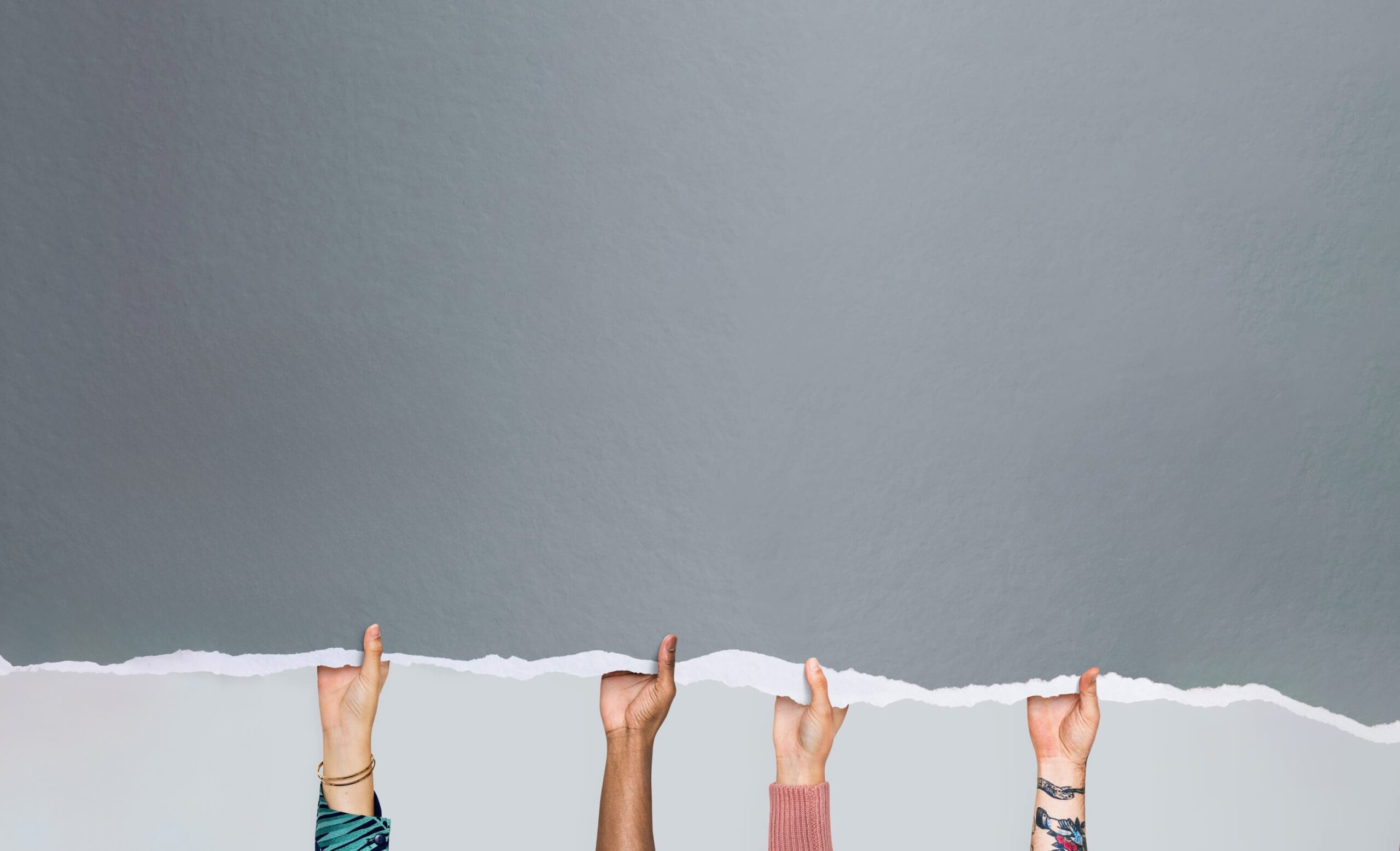 Vier verschiedene Hände halten von unten eine gezackte Papierkante hoch. Kleidung und Hautfarben variieren.